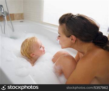 Mother and baby washing in foam filled bathtub