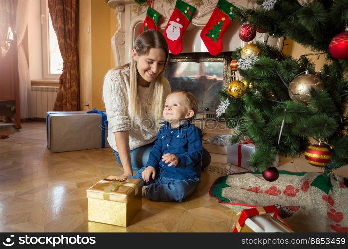 Mother and baby with Christmas gifts on floor at living room