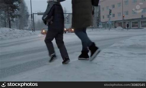 Mother and child crossing the road in winter city as cars stop at red signal of traffic lights