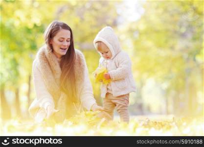 Mother and child in autumn park. Mother and child having fun in autumn park among yellow leaves