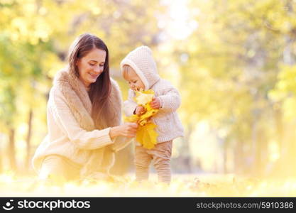 Mother and child in autumn park. Mother and child having fun in autumn park among yellow leaves