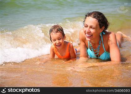 Mother and child lies in wave on shore