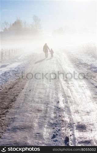 Mother and child on foggy snow road near farm