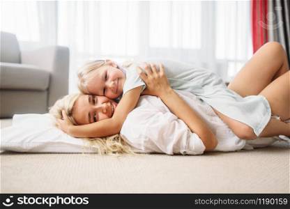 Mother and child play together lying on the floor at home. Parent feeling, togetherness, happy family