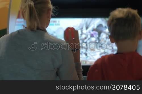 Mother and child playing on arcade machine in the amusement park. They throwing balls to the screen