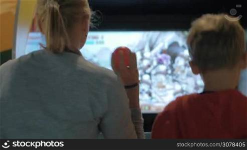 Mother and child playing on arcade machine in the amusement park. They throwing balls to the screen