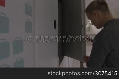 Mother and child putting travel bag into the locker of baggage room and paying, boy inserting coins