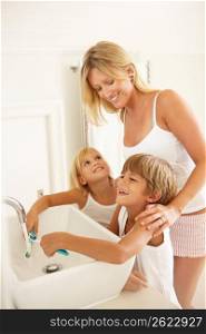 Mother And Children Brushing Teeth In Bathroom Together
