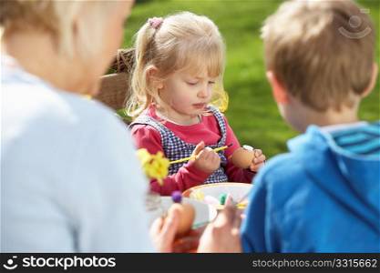 Mother And Children Decorating Easter Eggs On Table Outdoors