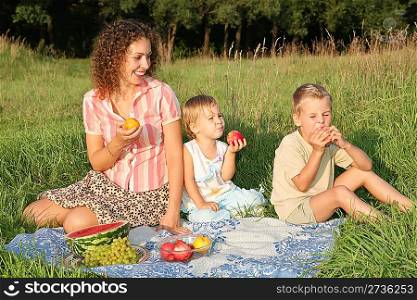 mother and children eat fruits sitting on the grass