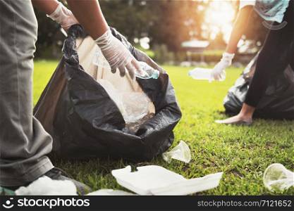 mother and children keeping garbage plastic bottle into black bag at park in morning light