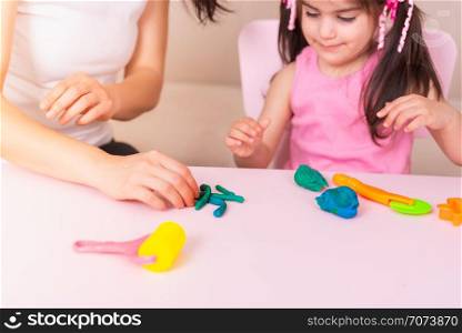 Mother and cute girl playing together with playdough while sitting on table.Selective focus and small depth of field.. Mother and Cute girl playing with playdough