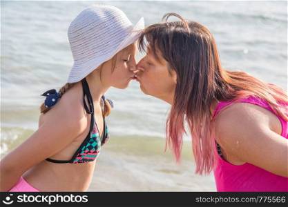 mother and daighetr are kissing on the beach in a summer day