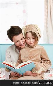 Mother and daughter (5-6) in bedroom reading book girl in bunny costume
