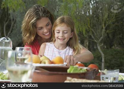 Mother and daughter (5-6) sitting at garden table, smiling