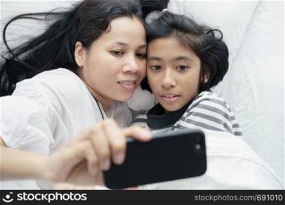 mother and daughter are taking a picture together. Asian women and cute girl so fun and happy to selfie on the bed.