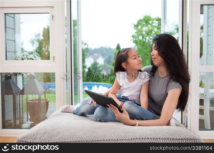 Mother and daughter at home with digital tablet, smiling at eachother