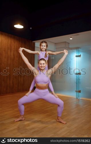 Mother and daughter, balance exercise in gym, yoga workout. Mom and little girl in sportswear, woman with kid on joint training in sport club. Mother and daughter, balance exercise in gym