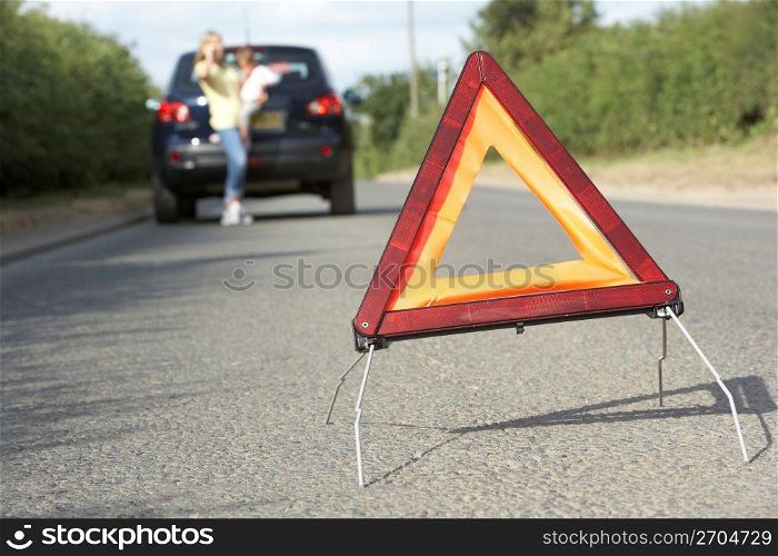 Mother And Daughter Broken Down On Country Road With Hazard Warning Sign In Foreground