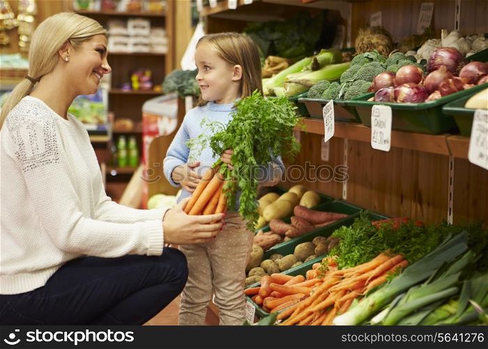 Mother And Daughter Choosing Fresh Vegetables In Farm Shop