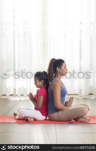 Mother and daughter doing yoga and meditating sitting back to back