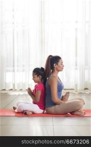 Mother and daughter doing yoga and meditating sitting back to back