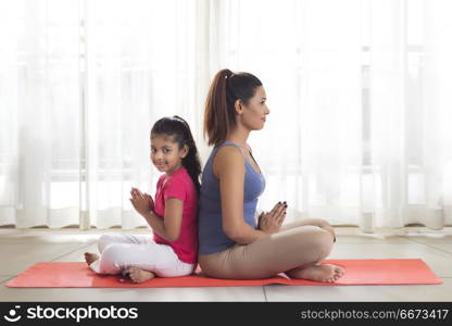 Mother and daughter doing yoga and meditating sitting back to back