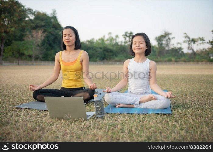 Mother and daughter doing yoga. woman and child training in the park. outdoor sports. healthy sport lifestyle,watching yoga exercises online video tutorial and meditation practice during work out.