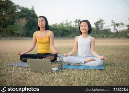 Mother and daughter doing yoga. woman and child training in the park. outdoor sports. healthy sport lifestyle,watching yoga exercises online video tutorial and meditation practice during work out.