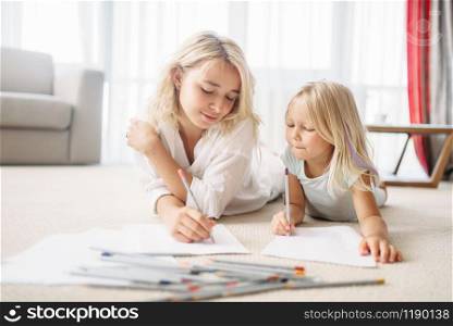 Mother and daughter draw with pencils lying on the floor. Parent feeling, togetherness. Mother and daughter draw lying on the floor