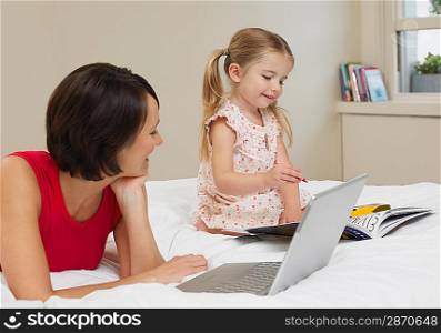Mother and daughter drawing and using laptop on bed