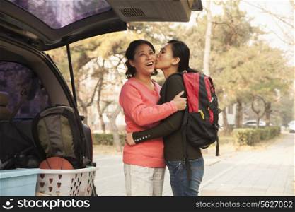 Mother and daughter embracing behind car on college campus