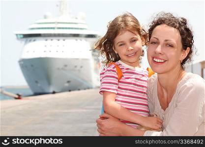 mother and daughter embracing, smiling and looking at camera, big cruise liner on background