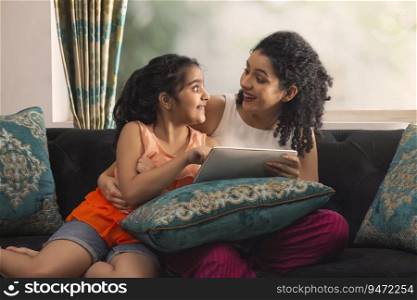 Mother and daughter enjoying together with tablet while sitting on sofa at home