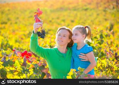 Mother and daughter family on autumn vineyard happy smiling holding grape bunch