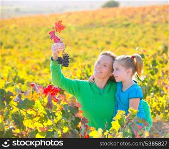 Mother and daughter family on autumn vineyard happy smiling holding grape bunch