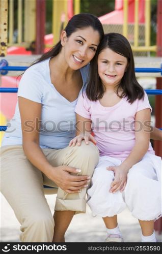 Mother and daughter girl sitting on playground structure smiling (selective focus)