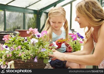 Mother And Daughter Growing Plants In Greenhouse