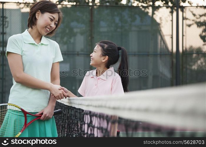 Mother and daughter handshaking over the tennis net