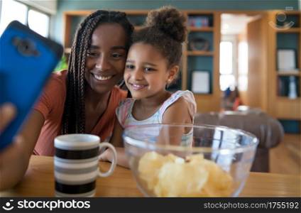 Mother and daughter having fun together and taking a selfie with mobile phone while staying at home. Monoparental concept. New normal lifestyle concept.