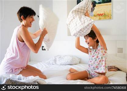 Mother and daughter having funny pillow fight on bed. Mum spending free time with her daughter.. Mother and daughter having funny pillow fight on bed.