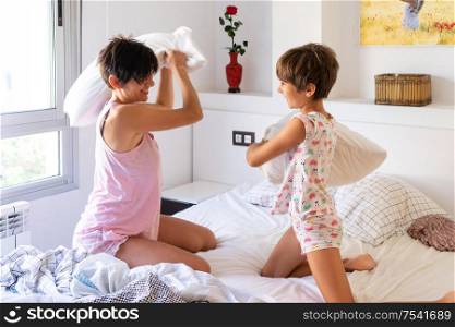 Mother and daughter having funny pillow fight on bed. Mum spending free time with her daughter.. Mother and daughter having funny pillow fight on bed.