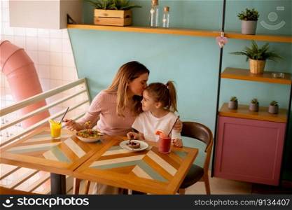 Mother and daughter having good time during breakfast with fresh squeezed juices in the cafe