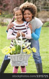 Mother And Daughter Holding Basket Of Daffodils In Garden