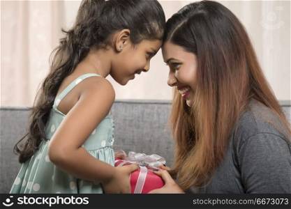Mother and daughter holding gift box and touching foreheads