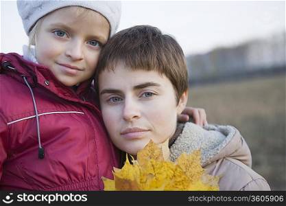 Mother and daughter holding leaves in field, portrait