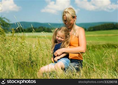 Mother and daughter in a sunlit meadow hugging each other