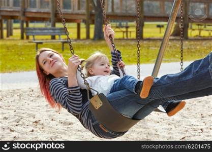 Mother and daughter in a swing having fun at the park playground