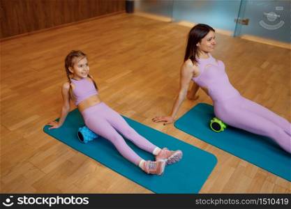 Mother and daughter in gym, exercise with massage rolls on mats, fitness workout. Mom and little girl in sportswear, woman with kid on joint training in sport club. Mother and daughter in gym, exercise with rolls