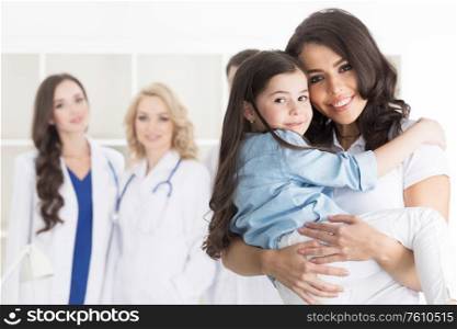 Mother and daughter in medical clinic, team of doctors on background. Mother and daughter in medical clinic